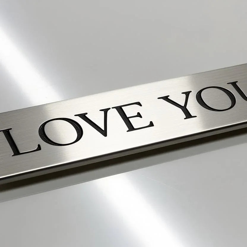 Close-up of a brushed metal plate with engraved black text 'LOVE YOU' on a reflective surface