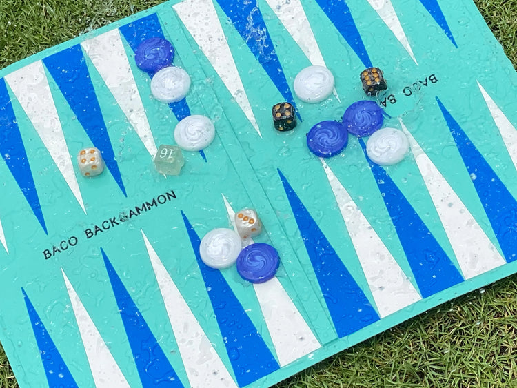 Baco Backgammon set outdoors with blue, white checkers and black, white dice on turquoise board with rain droplets